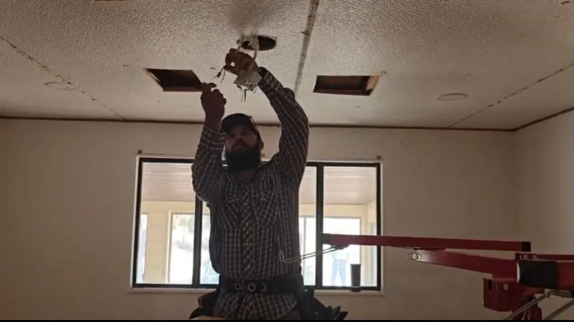 A worker repairs a ceiling inside a building while standing on a lift.