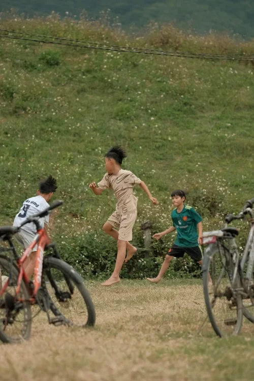 Children running and playing beside bicycles in a grassy mountain setting.